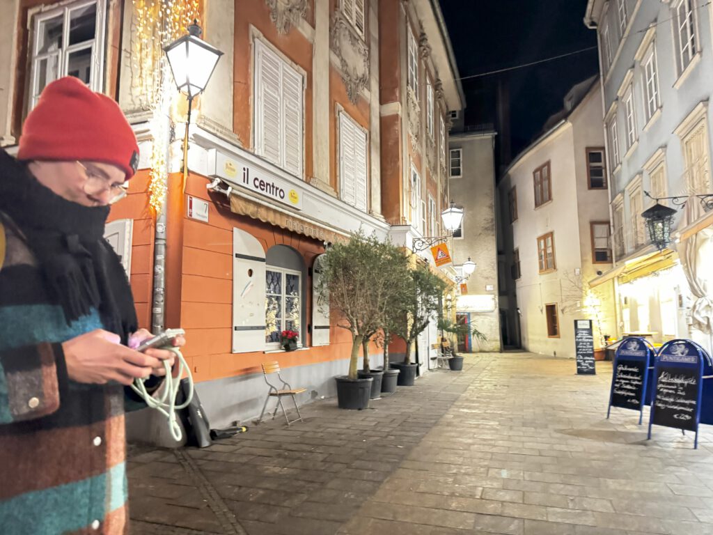 Zu sehen ist ein orange farbenes Haus in einer Gasse in Graz. Davor stehen Olivenbäume in Kübeln.