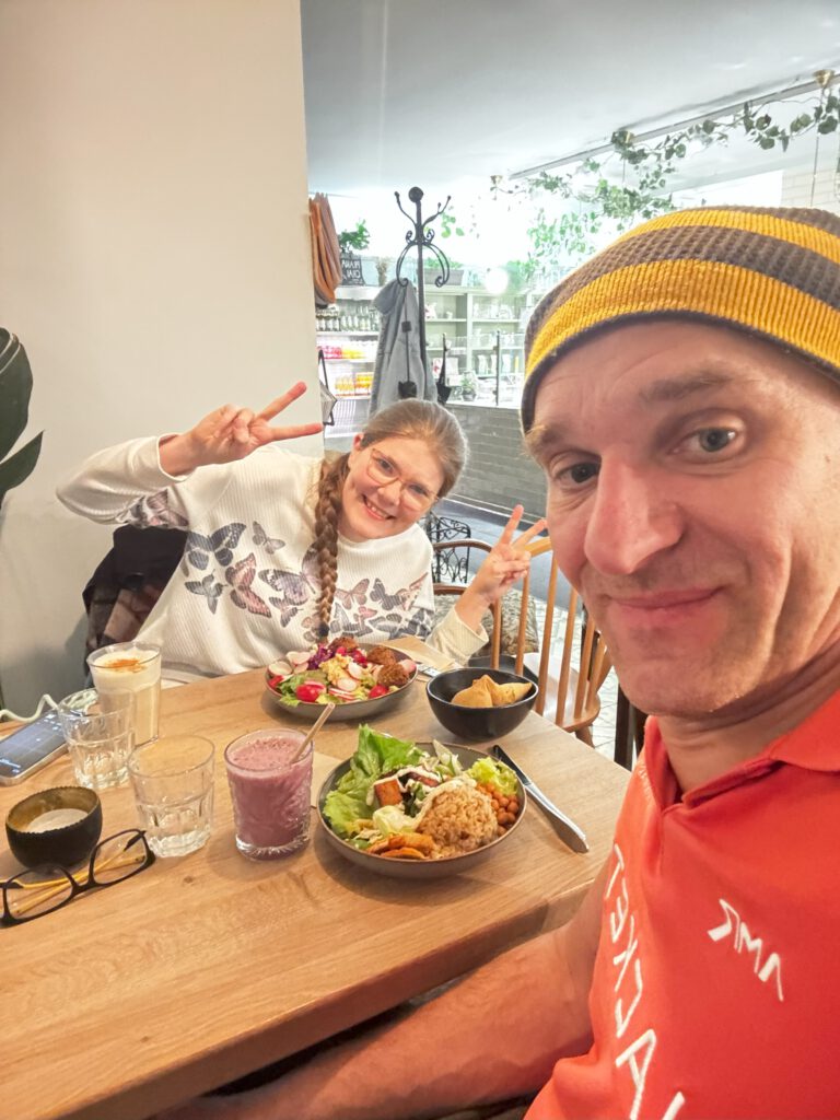 Zu sehen sind zwei Menschen in einem veganen Restaurant in Graz. Sie lächeln beide in die Kamera. Auf dem Tisch steht essen und Getränke.