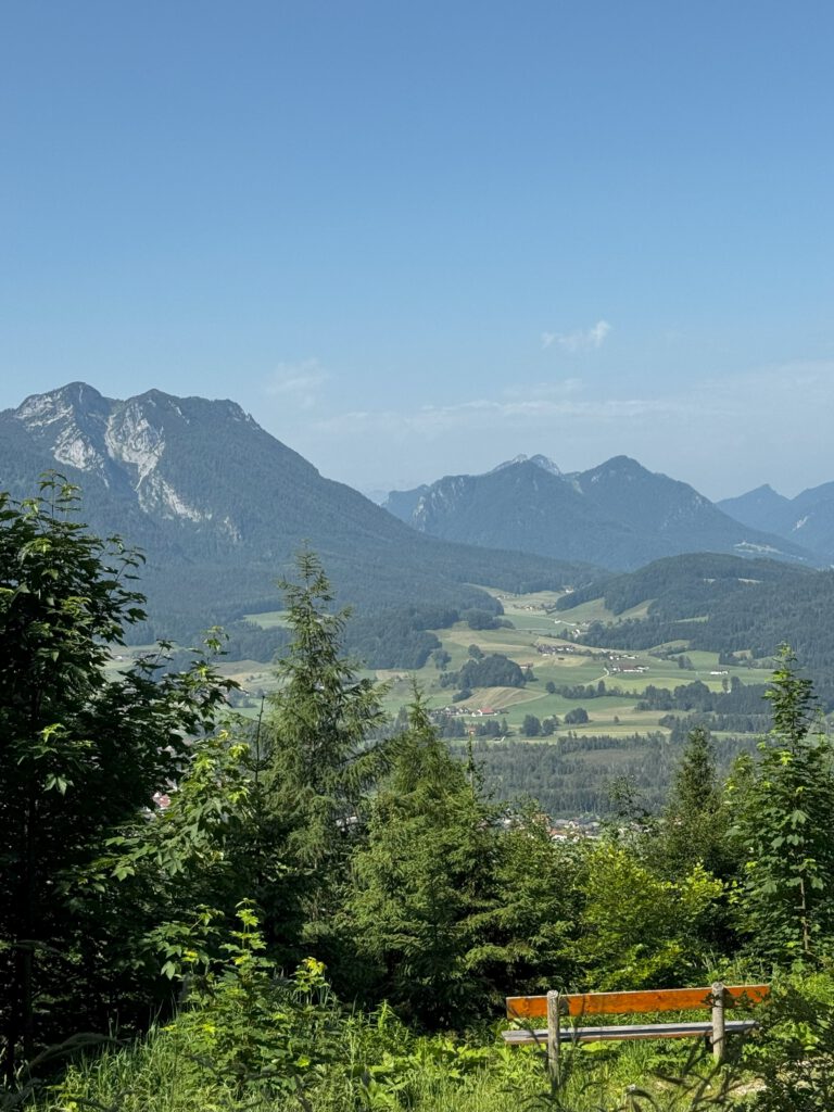 Blick auf die umliegenden Berge vom Wanderweg, welcher in Richtung Bäckeralm führt. Im Vordergrund ist eine Aussichtsbank.